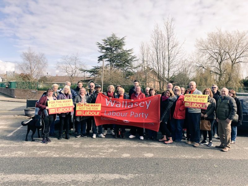 An outside view of Angela Eagle and around 25 Labour party members, some holding placards, standing behind the Wallasey Labour Party banner.  